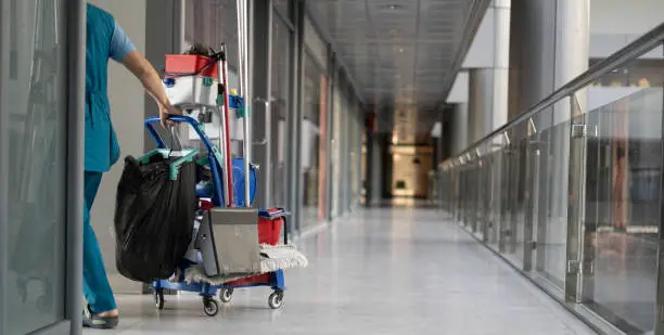 Photo of An employee pulls a trolley for cleaning offices. Woman cleaner is engaged in work.