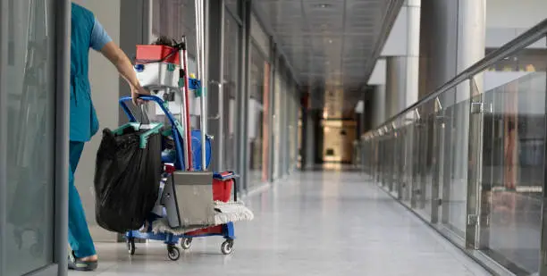 An employee pulls a trolley for cleaning offices. Woman cleaner is engaged in work. Shopping center place for text