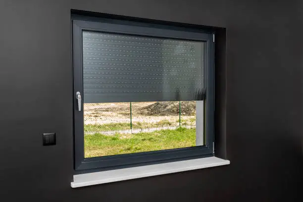Photo of A large window in a room with black walls, half covered with external blinds.