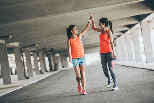 Two young woman giving high five to each other.They relaxing after jogging on street.