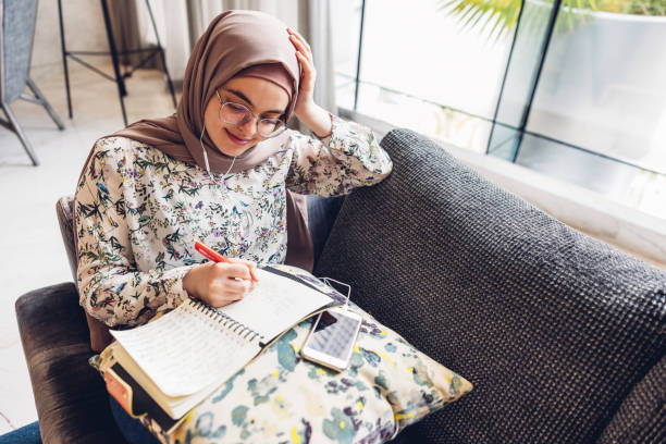 millennial girl confortavelmente sentado no sofá ouvindo música e fazendo anotações - arab style audio - fotografias e filmes do acervo