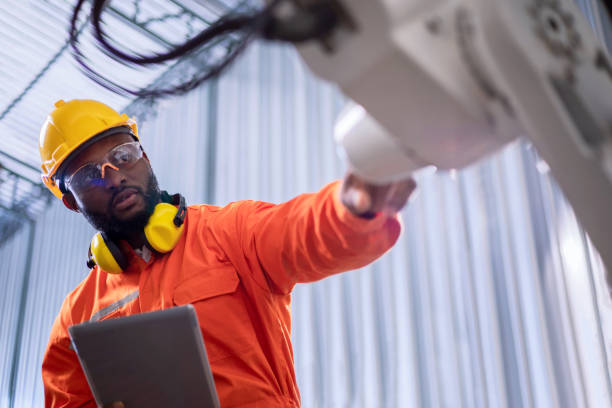 ingénieur africain pointant vers un bras robotique et retenait une tablette dans sa main. - safety sign protective workwear factory photos et images de collection