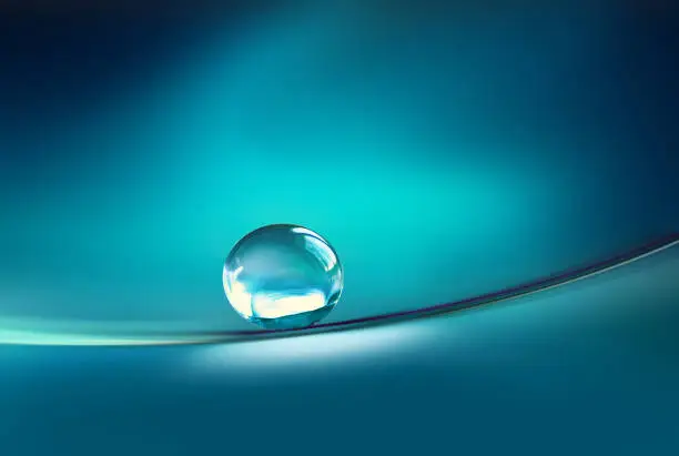 Photo of Beautiful transparent drop of water on smooth surface in dark blue colors.