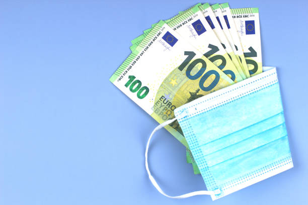 istock Some one hundred euro banknotes wrapped in disposable protective surgical face mask on light gray background. Top view 1316482092