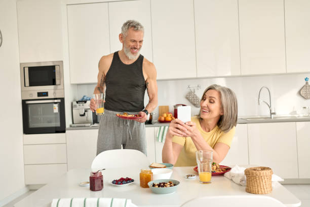 istock Happy older mature family couple having breakfast using phone in kitchen. 1316482995