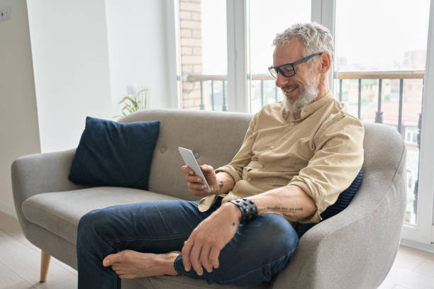 istock Happy older middle aged man using phone relaxing sitting on couch at home. 1316483029