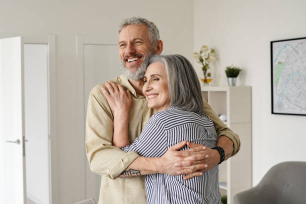 feliz pareja madura abrazándose, mirando hacia otro lado, pensando, soñando con el futuro en casa. - men middle senior adult human age fotografías e imágenes de stock