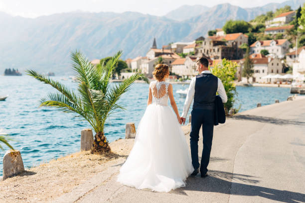 narzeczeni idą ręka w rękę na drodze nad morzem w pobliżu starego miasta perast, widok z tyłu - wedding beach bride groom zdjęcia i obrazy z banku zdjęć