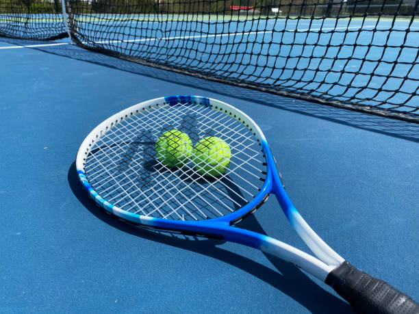Tennis racket on top of two tennis balls on a blue court by the net stock photo