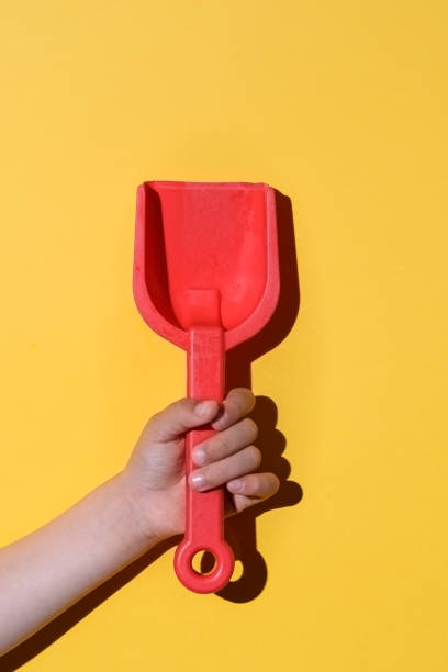 pala de juguete rojo en las manos de un niño caucásico con fondo amarillo - hand shovel fotografías e imágenes de stock