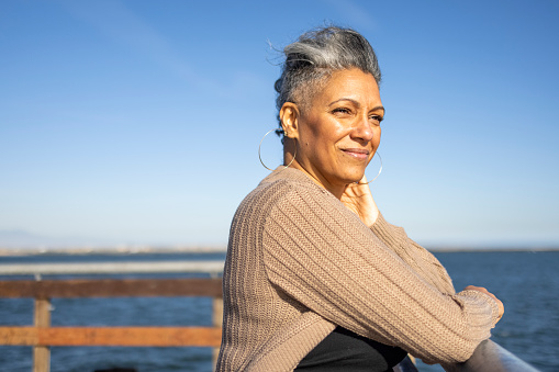 A mature black woman relaxes on the pier at the beach.