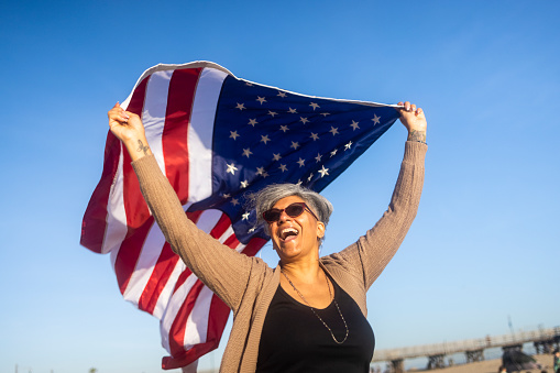 A happy black woman carrying and waving an American Flag at the beach.