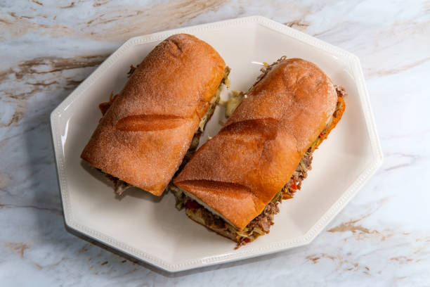 Messy Philly Cheesesteak Messy Philly cheesesteak with melted cheese mushrooms onions and peppers torpedo sandwich stock pictures, royalty-free photos & images
