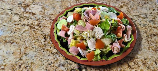 Large, Antipasto Salad, Isolated and Close Up; Delicious Food Large and oversized traditional Italian antipasto salad on a large round serving dish which includes Italian meats and cheeses and a variety of vegetables. antipasto stock pictures, royalty-free photos & images