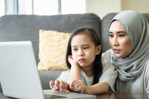 istock Young mother using laptop with her daughter on her lap Homeschool virtual internet online class 1316496882