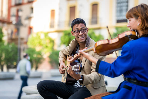 musiker paaren spielen und spaß auf der straße. lateinischer gitarrist und kaukasischer geiger. - street musician stock-fotos und bilder