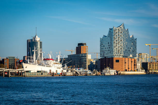 vista frontal de las hamburguesas más famosa sala de conciertos moderna junto a un barco de carga histórico con el überseebrücke y niederhafen en el fondo frente a la hafencity, hamburgo alemania - hamburg germany elbe river illuminated freight transportation fotografías e imágenes de stock