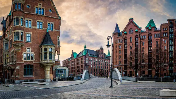 panoramic view of the Neuerwegsbrücke connecting St. Annenplatz with Sandtorkai in the speicherstadt, famous traditional warehouse district with typical brick facades during dusk in hamburg, germany.