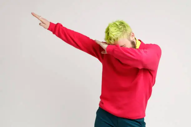 Photo of Photo of excited man with yellow hair, showing popular internet meme pose, celebrating success victory, dabbing trends, expresses positive.