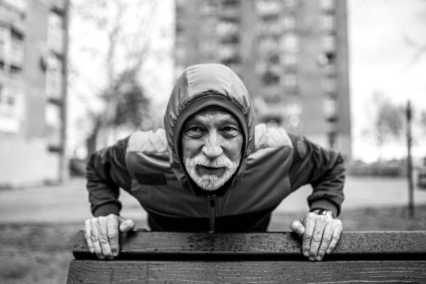 Sporty senior man doing push-ups on cold rainy day.