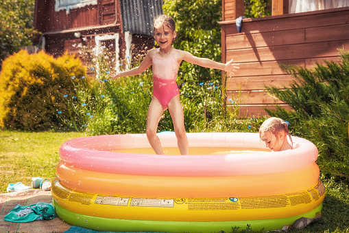 Happy playful children girls having fun outdoors in inflatable swimming pool in sunny summer day during summer holidays in countryside concept for happy childhood lifestyle