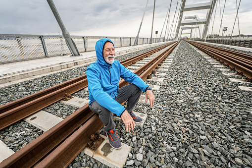 Senior sportsman resting on railroad tracks on a bridge.