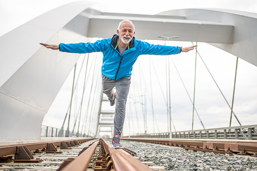 Happy senior sportsman standing on railroad and practicing body balance. Feels like flying.