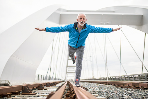 Happy senior sportsman standing on railroad and practicing body balance. Feels like flying.