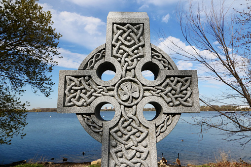 Stone Celtic cross with irish four leaf clover on waterfront in Kingston, Ontario, Canada. Celtic cross monument stock photo. \n\nThis cross was built to commemorate Irish immigrants who died during the construction of the rideau canal, a UNESCO world heritage site in Kingston Ontario Canada.