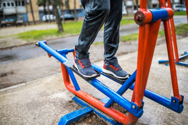 Legs close-up of senior man exercising outdoors on stepping machine.
