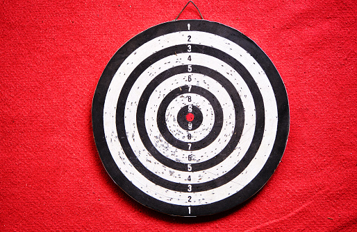 Used dart board standing on red carpet and its shadows.