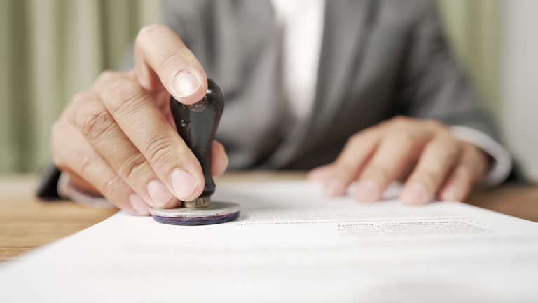 Close-up Of Businessman holding an Approved rubber stamp with document At Desk