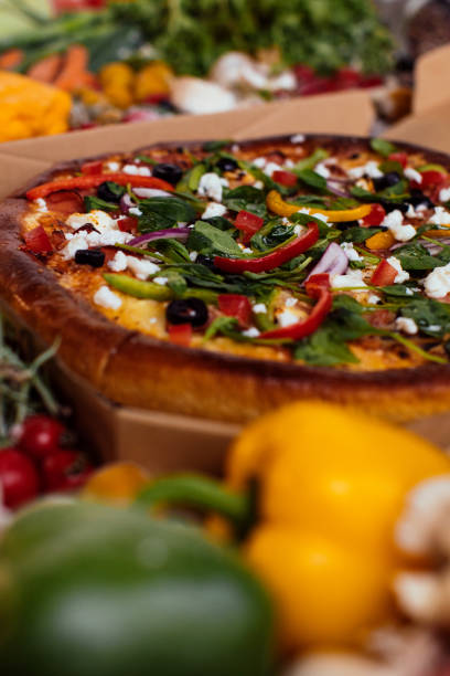 Vegetable and cheese pizza on a table surrounded by fresh ingredients
