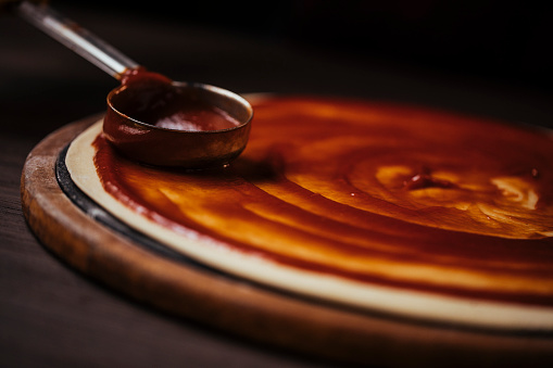 Close up shot of spreading marinara sauce on top of a pizza dough