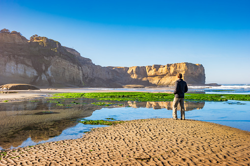 Hiker looks at view in Devils Punchbowl State Natural Area in Otter Rock, Oregon, USA