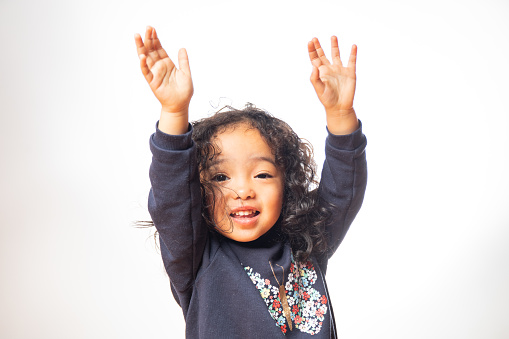 A young half Japanese half African American girl with frizzy hair and hands in the air on white background.