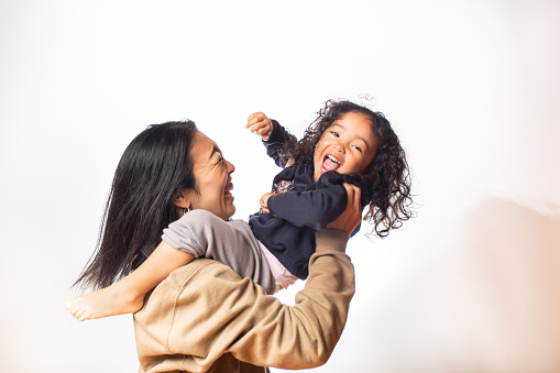 A young Japanese Mother and her mixed race young daughter having lots of fun together with very happy emotions on white background.