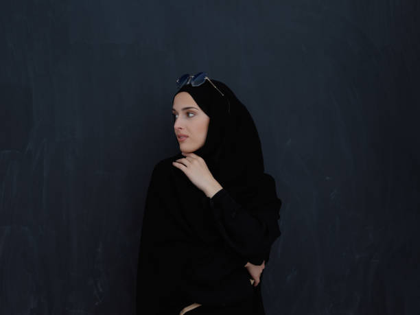 Young muslim in traditional clothes or abaya and sunglasses posing in front of black chalkboard Young muslim in traditional clothes or abaya and sunglasses posing in front of black chalkboard. Arab woman representing modern arabic lifestyle, islamic fashion and Ramadan kareem concept arabian sunglasses stock pictures, royalty-free photos & images