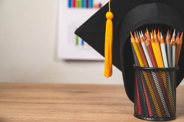 istock Graduate cap and a pen holder filled with colored pencils on table in library 1316535135