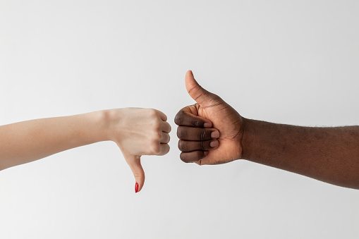 Like dislike gesture. Racial tolerance. Versus opposition. Gender diversity. Problem cooperation. Conceptual art. White female and black male hands showing thumbs up down isolated light.