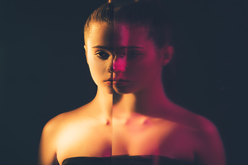 Bipolar disorder. Mental health. Depresion loneliness. Double exposure silhouette night half face portrait of apathetic woman with mirror reflection out of focus in pink neon light isolated on dark.