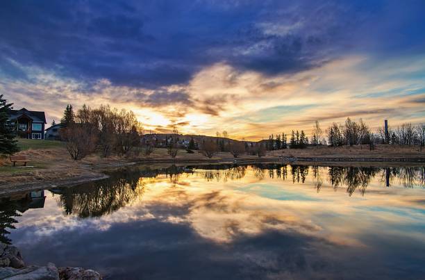 Sunrise Clouds Over A Park Lake A bright sunrise sky reflecting into a park lake in Cochrane. cochrane alberta photos stock pictures, royalty-free photos & images