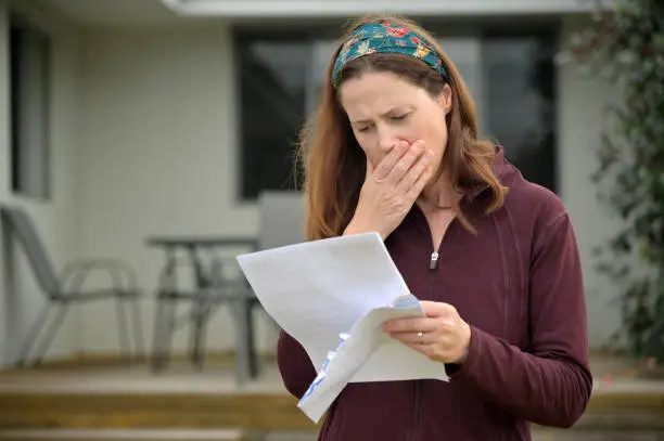 Photo of Upset woman reading a letter in home front yard