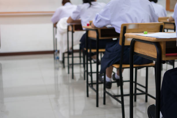 Asian High school or university student reading question exam test class and using pencil writing on paper answer sheet, doing final exam attending in examination classroom with students in uniform