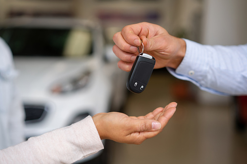 Primer plano de un vendedor dando las llaves de su coche nuevo a una pareja en el concesionario photo