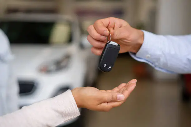 Photo of Close-up on a salesman giving the keys to their new car to a couple at the dealership