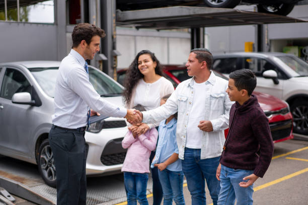 Salesman greeting a family interested in buying a car at the dealership Salesman greeting with a handshake a happy Latin American family interested in buying a car at the dealership - car ownership concepts car ownership photos stock pictures, royalty-free photos & images
