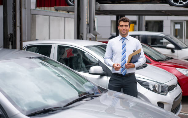 portrait of a salesman working at the dealership showing cars outdoors - professional dealer imagens e fotografias de stock