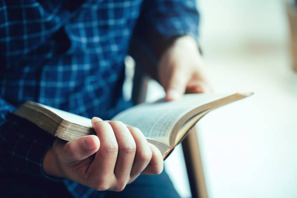 mann sitzt beim lesen von bibel oder buch über betonwand mit fensterlicht - praying god love wisdom stock-fotos und bilder