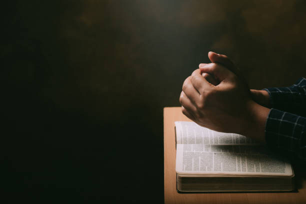 manos de orar joven y biblia sobre un fondo de escritorio de madera.hombre unir las manos para orar y buscar las bendiciones de dios, la santa biblia. - chapter one fotografías e imágenes de stock